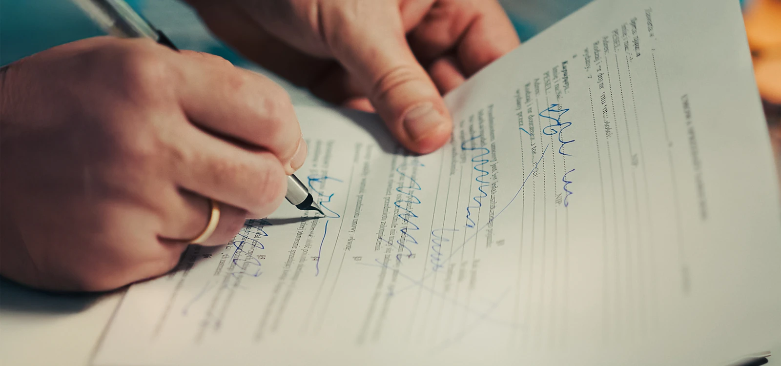 Two people filling in and signing a paper application together at a table