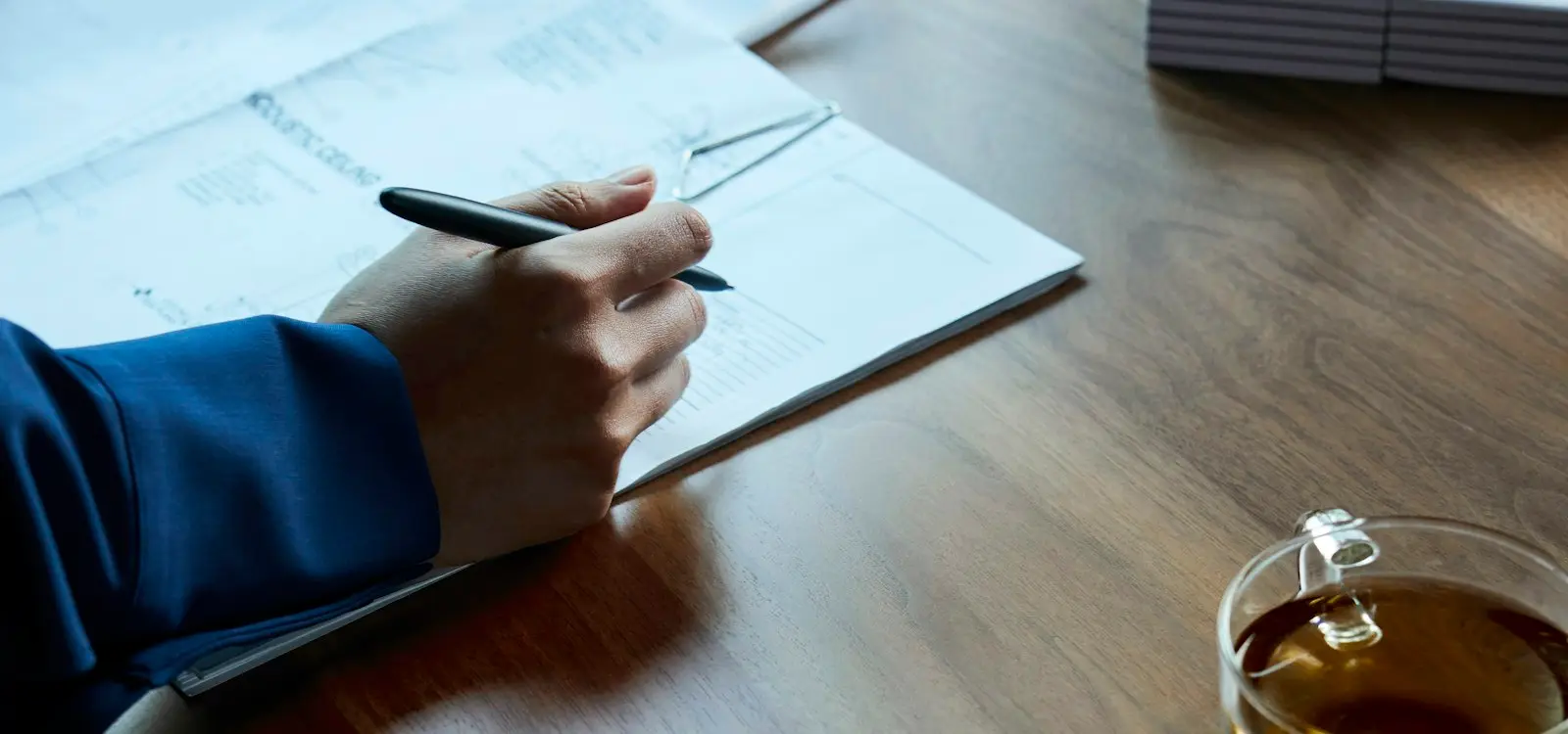 A hand filling in a printed form with a pen at a wooden table