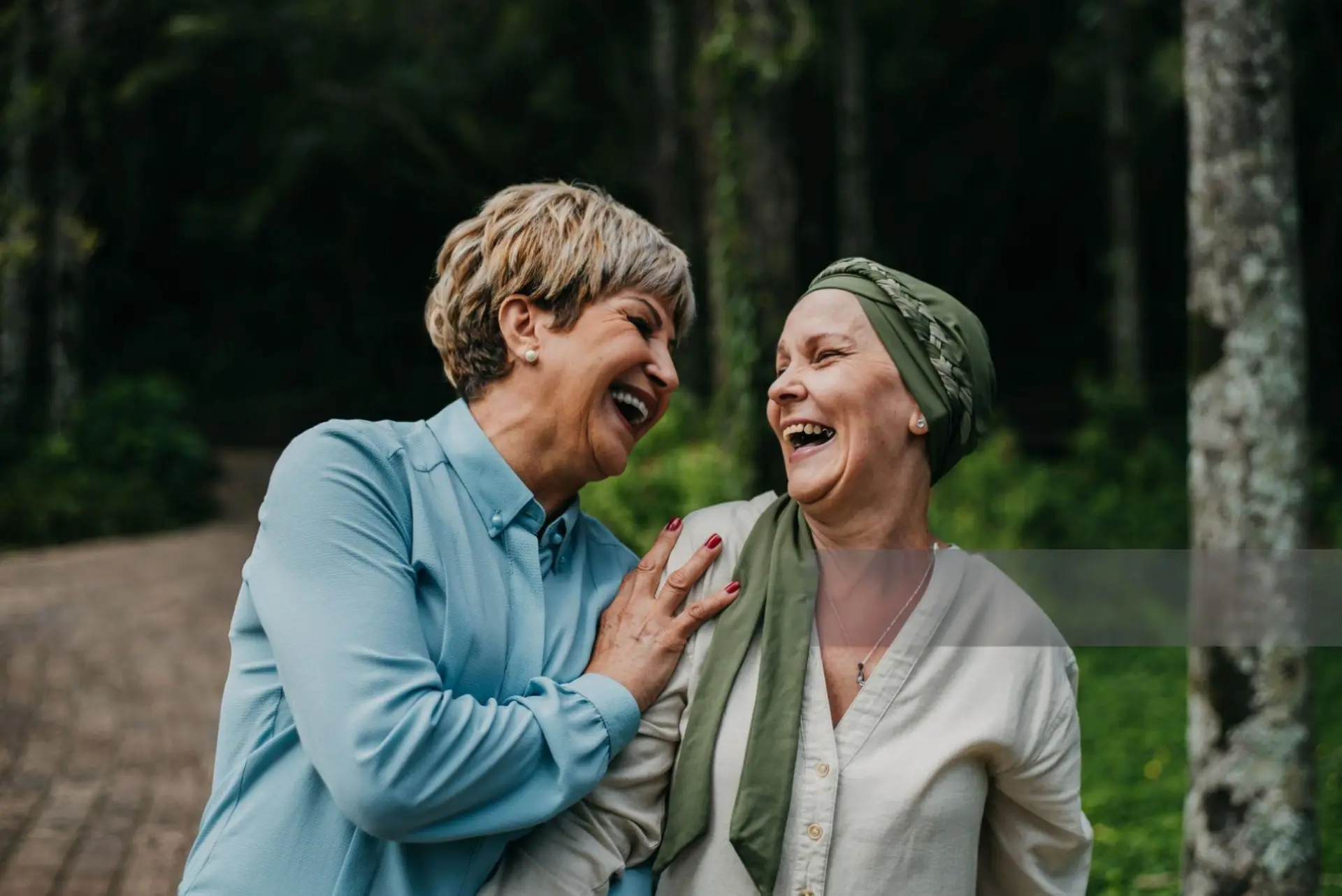 Two women laughing together, one wearing a headscarf during cancer treatment